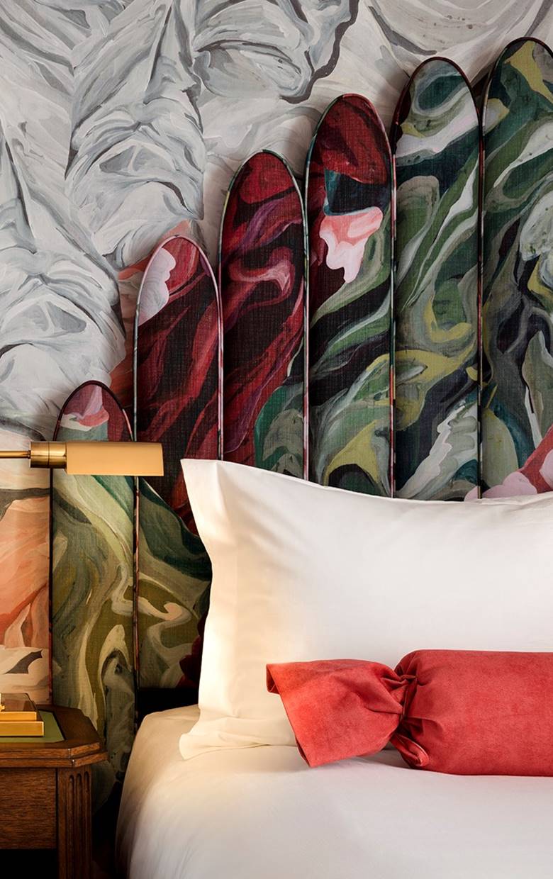A floral-patterned headboard with red, green, and pink contrasts against a white pillow and coral bolster at Riggs DC.